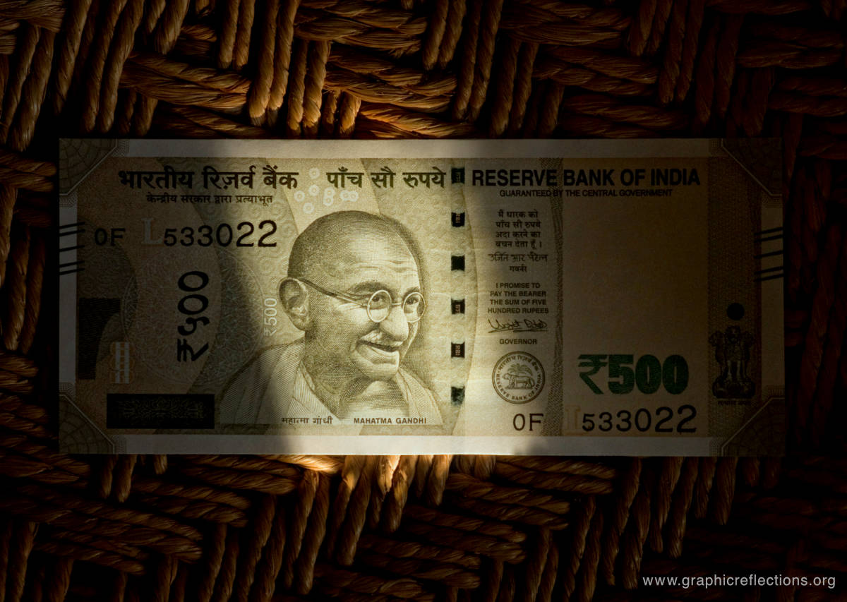 An Indian Rupee currency note in shade, with light falling on Mahatma Gandhi’s image printed on it